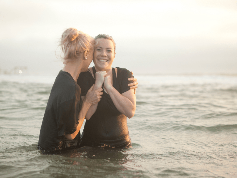 a young woman getting baptized outdoors by a fellow Christian.